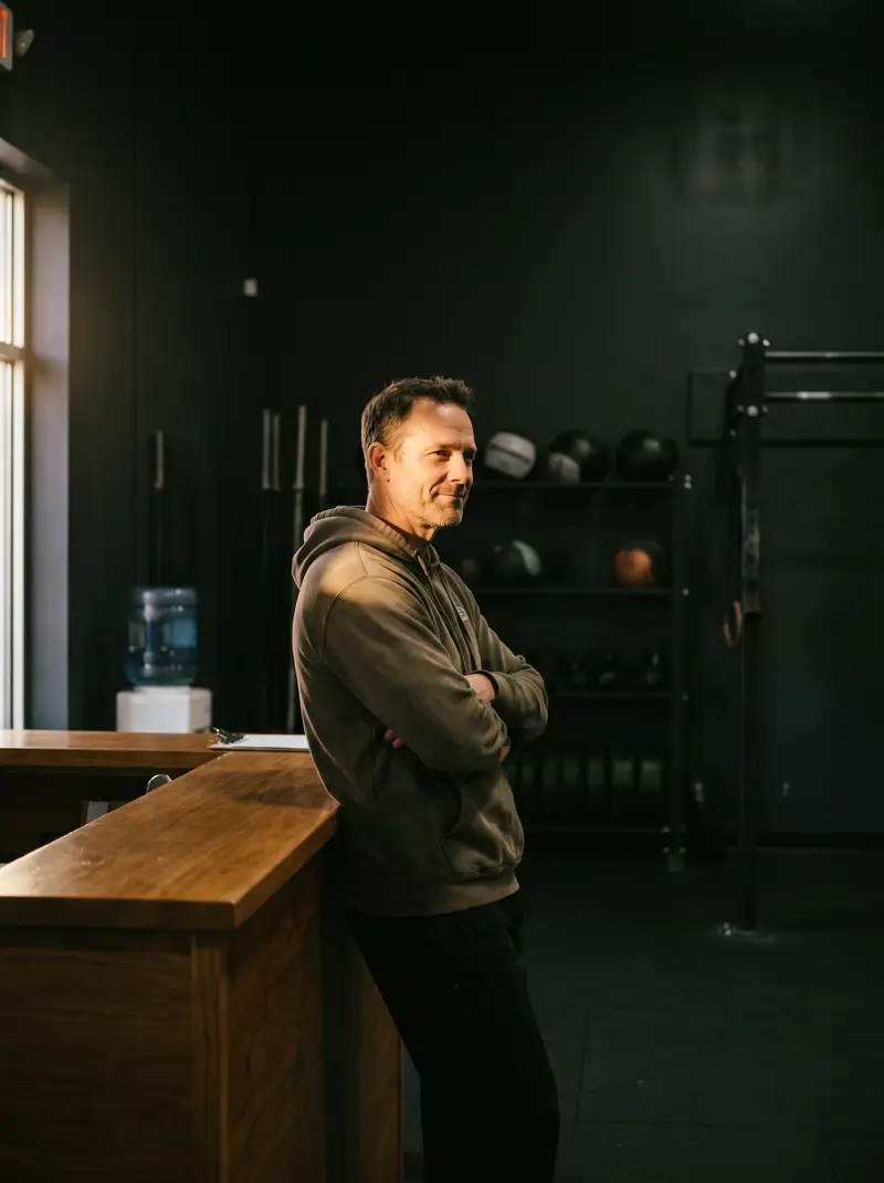 Dono da academia no balcão da recepção, com a luz da janela